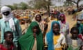 Sudanese children stare at the camera with a expanse of makeshift shelters behind them