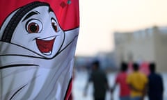 People walk at a beach near a banner of the Qatar 2022 mascot La'eeb in Doha