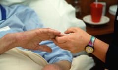 Hospice worker holding the hand of an elderly man.