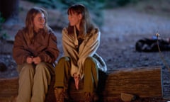 A girl sits on a log next to a woman.