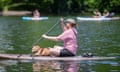 A man paddleboards with his dog with kayaks in the background.