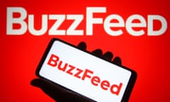 Hand holds phone with 'Buzzfeed' written in red on screen, behind red background with 'BuzzFeed' in white