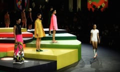 Models wearing yellow, pink and white mini dresses stand on a yellow, green and black stage