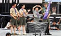 Two South Korean scouts  stand on stage next to two Polish scouts, one of whom is making a hand-heart gesture while the other holds the scout flag