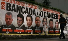 A person walks past a poster with the phrase 'They want more poison in your food. Cancer caucus' depicting Brazil’s deputies who voted for a law that facilitates the registration of pesticides