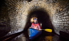 Gordon McMinn illuminated while in a canoe in a dark tunnel