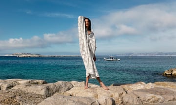 Female model wearing a off-white broderie anglaise midi-length dress in front of the sea.