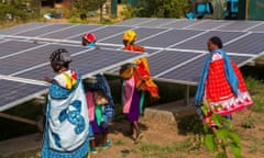 Women wearing brightly coloured prints walk through rows of solar panels.