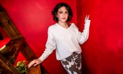 Emily Wilson standing next to wooden stairs at her home in New York, a red wall behind her