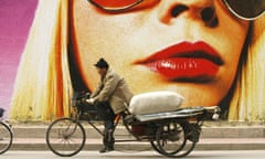 A man delivering goods passes a fashion billboard in Beijing, China