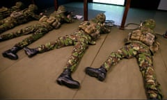 Army recruits lie prone on a floor aiming computerised guns at a screen