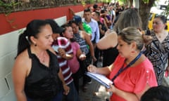 People wait in line against a wall to talk to a woman with a notebook and lanyard