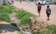 Schoolchildren walk past flowing sewage in a storm drain in Chitungwiza, Zimbabwe