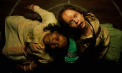 Two possessed girls with scarred faces and creepy eyes stare up at the camera as they sit back to back, their heads resting on each others' shoulders.