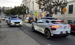 Two driverless Waymo taxis face off on a street in San Francisco before driving past each other.