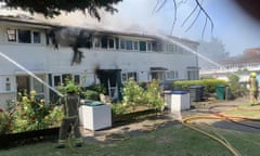 Two firefighters point hoses at the row of white panel-clad homes