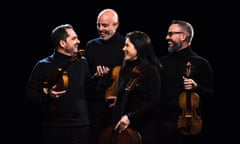 the four players of the Cuarteto Quiroga wearing black, against a black background, holding their instruments while turning to each other and smiling