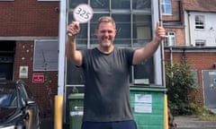 Simon Squibb, smiling and standing in front of the disused staircase, holds up an auction paddle and makes a thumbs-up gesture