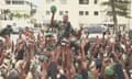 Man in military uniform with green cap in one raised hand amid mostly uniformed arms holding up cameras