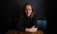 Tim Minchin sits at a table in front of a black wall