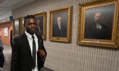 Joseph-Christopher Luamba walks through courthouse lined with pictures of judges.