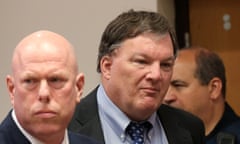 Man with toupee and blue shirt stands between two officials in court