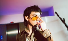 Declan McKenna has his finger to his sunglasses in a posed shot.