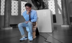 A man sitting (fully clothed) on a toilet with his head leaning on his right fist
