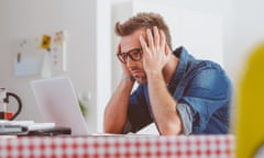 Worried man looking at the laptop screen<br>Worried man wearing jeans shirt and nerd glasses sitting at the table, holding head in hands, looking at laptop screen.