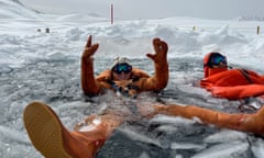 two people in dry suits in hole in frozen lake