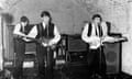 Grainy black and white photos of the three of the Beatles, with no drummer visible, playing in a club with a low vaulted roof