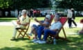 Older people in deck chairs  in shade with twoo younger people walking past