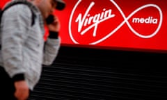 A man on a mobile phone passes a Virgin Media sign