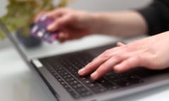 A person using a laptop as they hold a bank card.