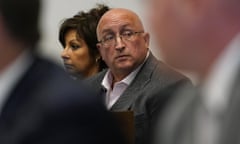 A bald man wearing glasses sits in a courtroom.