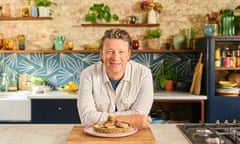 Jamie Oliver smiling and leaning on the counter in front of a wooden board with a fig tart on top of it.