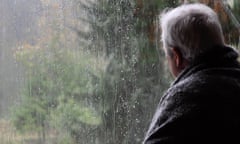 Man wrapped in a blanket looking out of a window on a rainy day