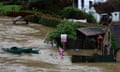 Bowed Union Jack flags and a for sale sign are seen in turbulent flood water risen around a home with three nearby boats floating high in the water