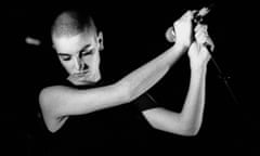 A black and white image of Sinéad O'Connor looking downwards with a microphone held at arm's length level with her head.