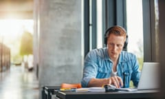 University student working on academic assignment<br>Portrait of young student wearing headphones sitting at the table in library and reading book. University student finding information for his academic assignment.