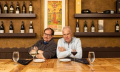 Jason and Paul sitting at a restaurant table with their arms folded and looking very serious