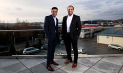 Mohsin and Zuber Issa standing side by side outdoors on a balcony, with a carpark and buildings behind them