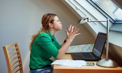 A side-on view of a woman grimacing at her desk in front of a laptop and smartphone