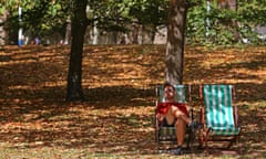 A man sits on a deckchair among brown leaves fallen from the trees in St James' Park in London in August.