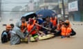 Rescuers assist residents on a boat as they wade through a flooded road