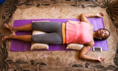 Stock image: a woman lying on the floor using a meditation app on her phone.