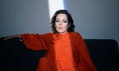 Olivia Colman in orange dress on brown sofa, with shaft of light coming down across her face