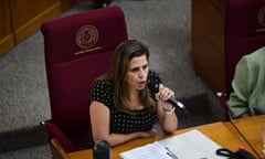 A woman who is seated on a maroon chair speaks into a mic