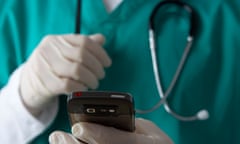 man wearing medical scrubs and stethoscope holding mobile phone checking messages<br>BHXB1F man wearing medical scrubs and stethoscope holding mobile phone checking messages