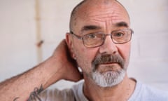 Close-up of Andrew Malkinson with greying, neat beard, glasses and cropped hair, as he puts right hand behind head